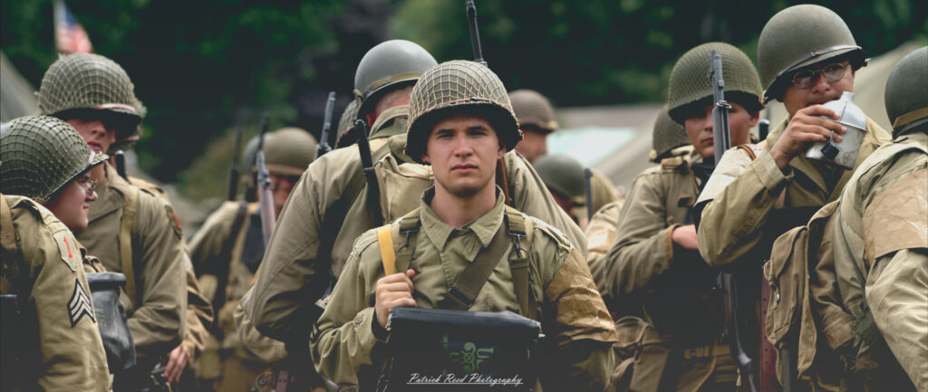 A soldier standing in ranks, staring straight ahead with a focused expression. Dressed in uniform, his posture is straight and disciplined, embodying the ideals of duty and commitment as part of a larger military formation.